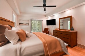 A bedroom with a bed, a television, a mirror, a dresser, and a ceiling fan.