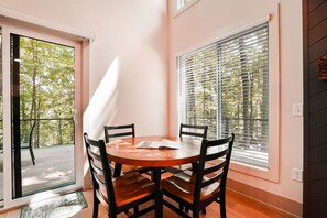 A dining area with a round table, four chairs, a door leading outside, and a window with blinds.