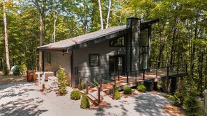 A modern cabin with a deck, surrounded by trees. - Onyx Ridge | Hocking Hills, Luxury Cabin, Hot Tub (South Bloomingville)