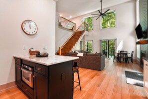 Une cuisine moderne dotée d’un îlot central, d’un coin repas avec une table et des chaises, d’un escalier et d’une grande fenêtre qui laisse entrer la lumière naturelle.