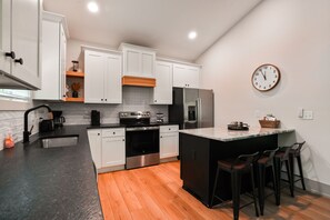 A modern kitchen with white cabinets, a stainless steel refrigerator, a built-in oven, and a large island with bar stools. - Onyx Ridge | Hocking Hills, Luxury Cabin, Hot Tub (South Bloomingville)