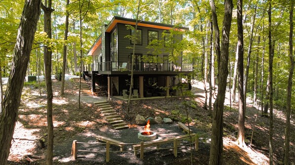 A modern cabin with a deck, surrounded by a forest.