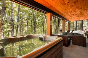 A hot tub with a view of a forest, wooden ceiling, and wicker furniture.