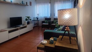 A living room with a TV, sofa, lamp, and a small table with decorative items. - Peniche Nature and Beach Flat (Peniche)