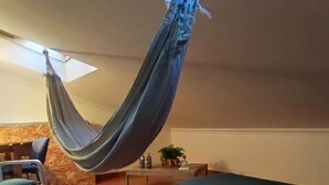 A hammock suspended from the ceiling in a living room with tiled flooring, a sofa, and a small table with decorative items. - Peniche Nature and Beach Flat (Peniche)