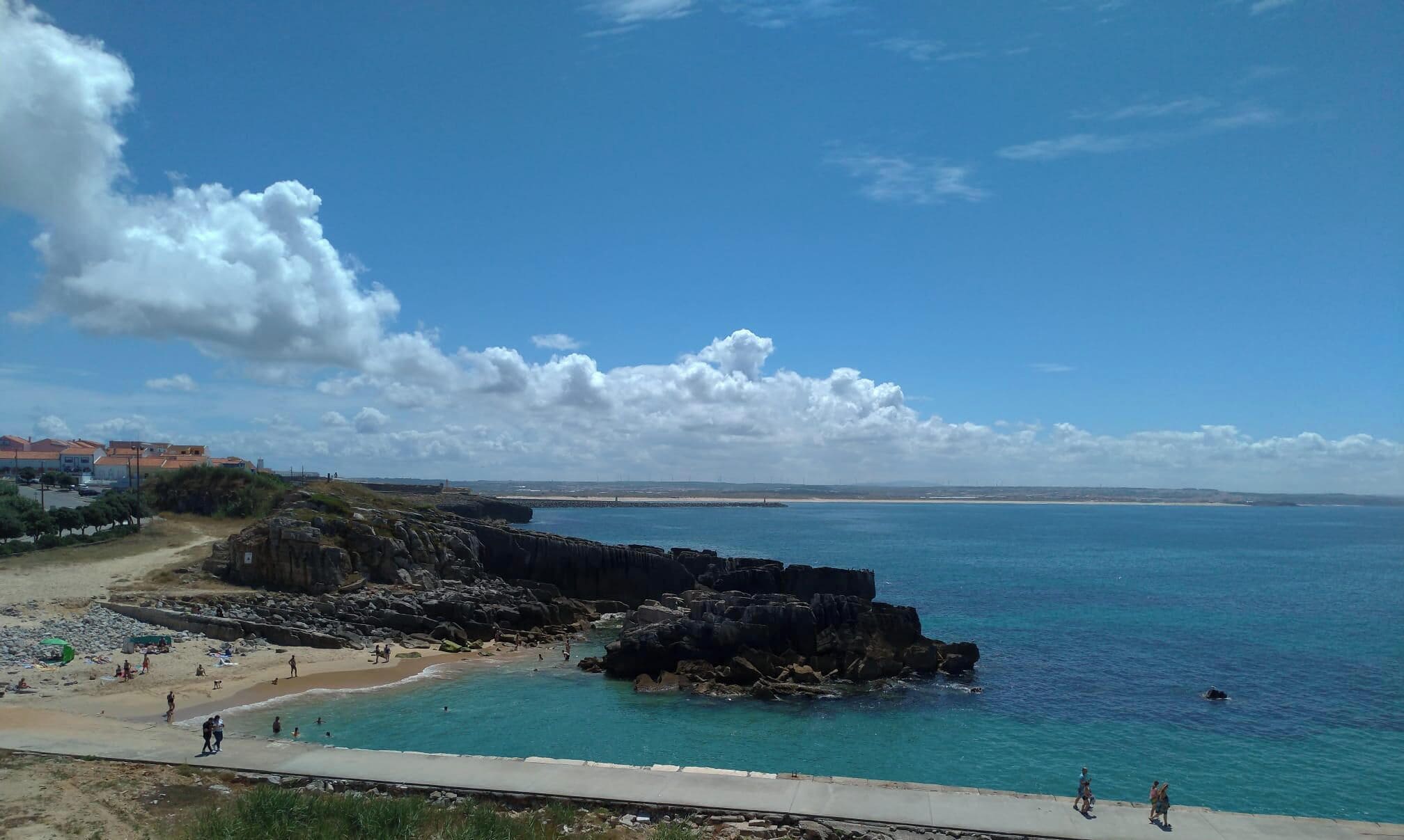 Une plage côtière avec des affleurements rocheux et une mer d’un bleu limpide.