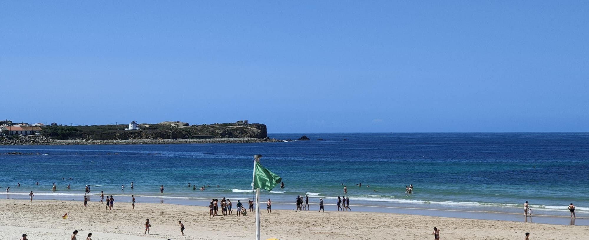 A beach with people, a lighthouse, and a rocky coastline.