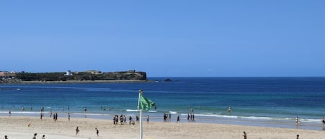 A beach with people, a lighthouse, and a rocky coastline.