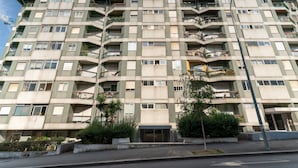 En flervåningsbyggnad med bostäder, balkonger, en central entré och en gata framför.