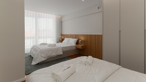 Ett hotellrum med två sängar, en garderob, ett nattduksbord med en lampa och ett fönster med tunna gardiner.