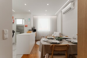 A modern dining area with a table set for two, a kitchen in the background, and an air conditioning unit mounted on the wall. - Apartment 'Fernão De Magalhães' with Balcony, Wi-Fi and Air Conditioning (Porto)