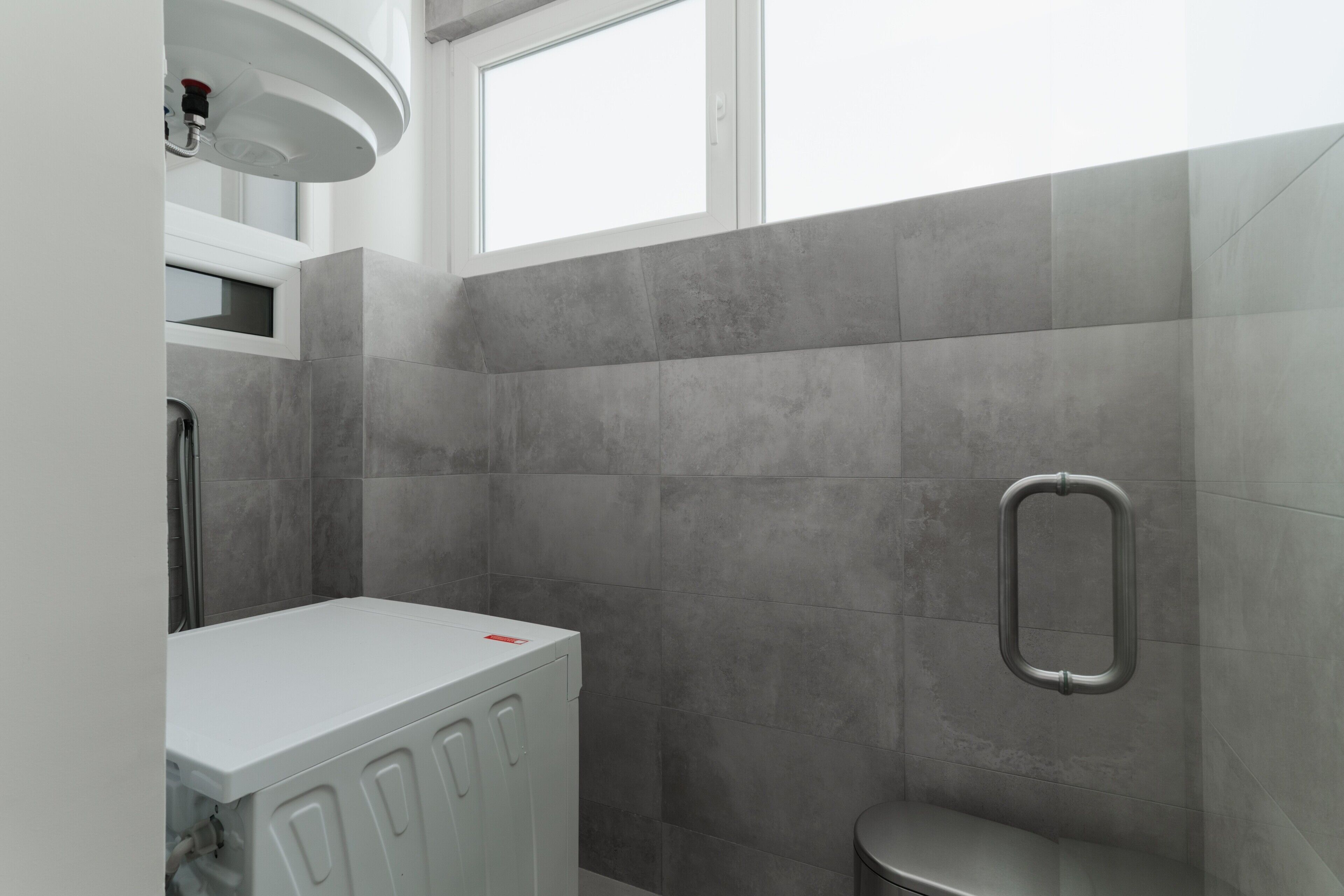 A bathroom with grey tiles, a white sink, and a window.
