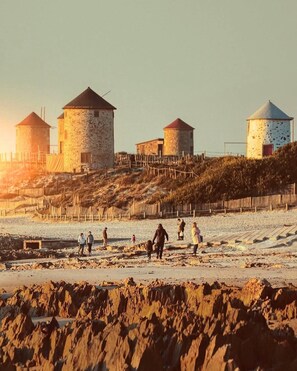 A coastal scene with stone windmills and a sandy beach. - Apulia Garden Barbecue Suite (Esposende)