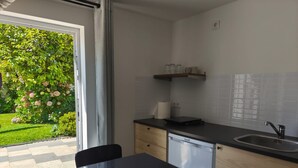 Cocina compacta con lavavajillas, un lavabo y una pequeña encimera. Hay una ventana con vistas a un jardín.