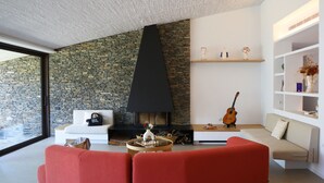 A modern living room with a stone wall, a fireplace, a red sofa, a coffee table, and a bookshelf.