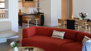 A modern living room with a red sofa, a chessboard, and a dining area with a table and chairs.