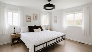 A bedroom with a bed, bedside tables, a hanging light fixture, and framed artwork on the walls.