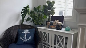 A wicker chair with a blue cushion and an anchor pillow, a white cabinet with glass doors, and a potted plant with large green leaves.