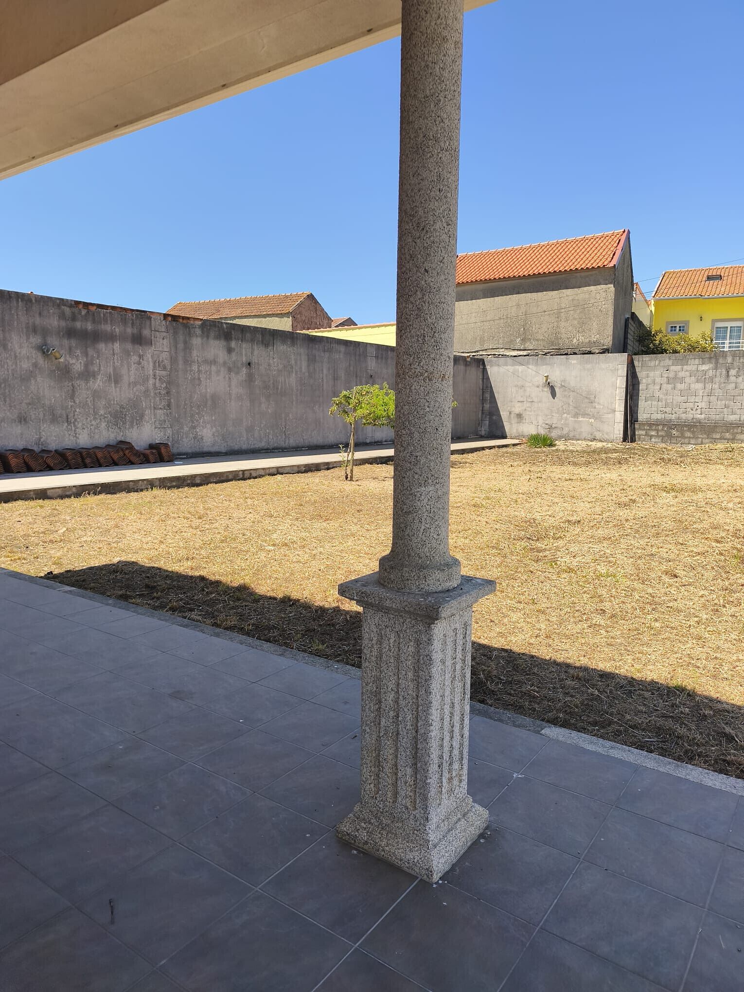 Un patio con una columna de piedra, suelo de baldosas y pared de concreto.