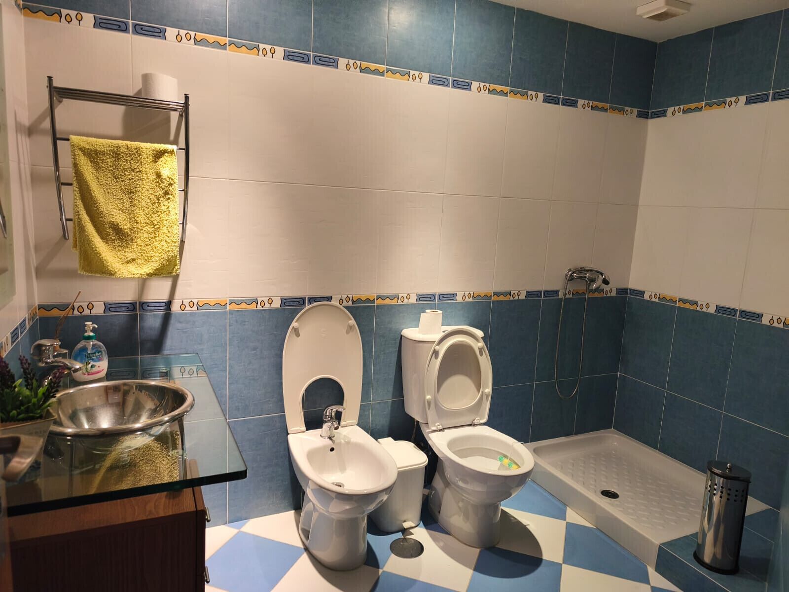 Un baño con dos inodoros, un bidé, un lavabo de vidrio y una ducha.