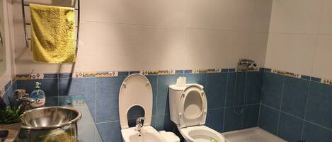 Un baño con dos inodoros, un bidé, un lavabo de vidrio y una ducha.