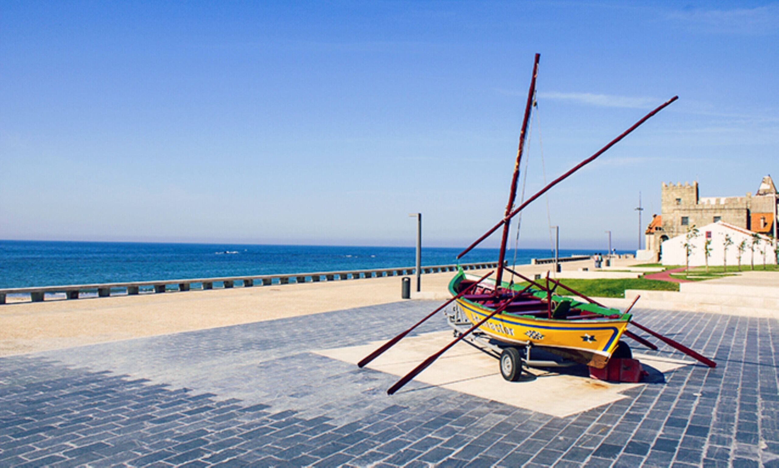 A colorful boat on a paved area near a body of water and a historic building.