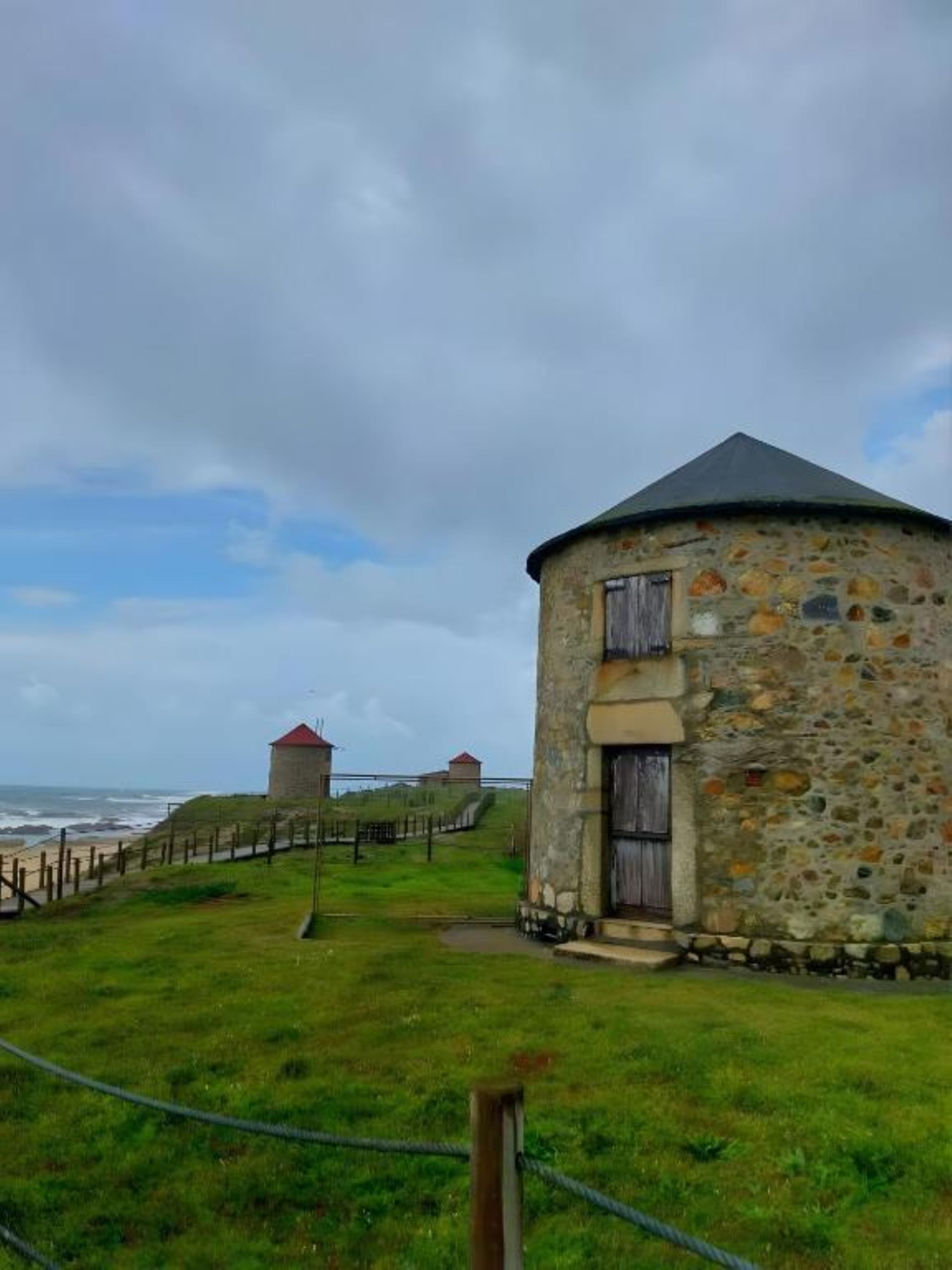 A stone building with a circular design, a wooden door, and a small window. There is a grassy area in front with a fence and a path leading to the building.