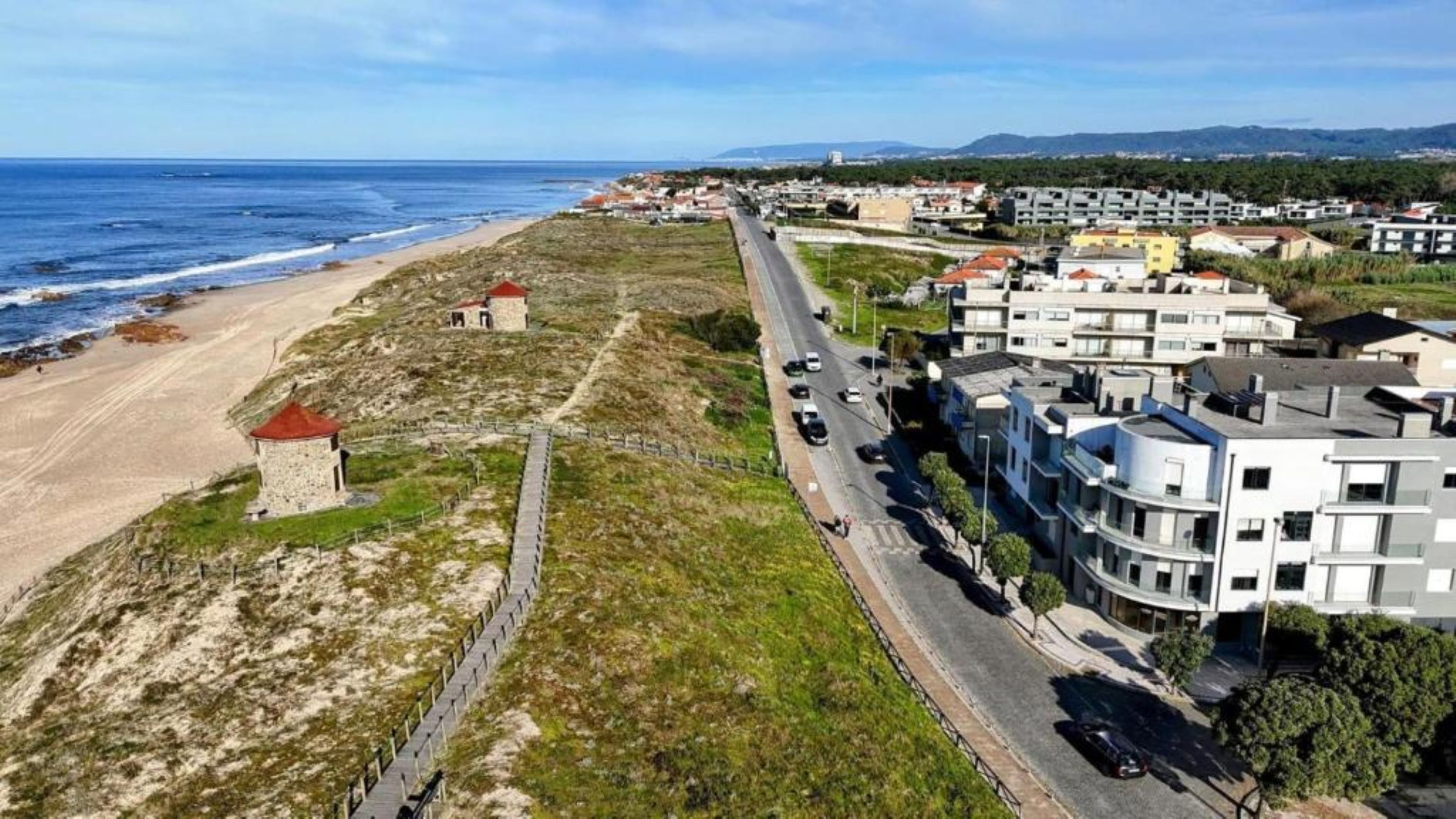 A coastal road with buildings and a beach.