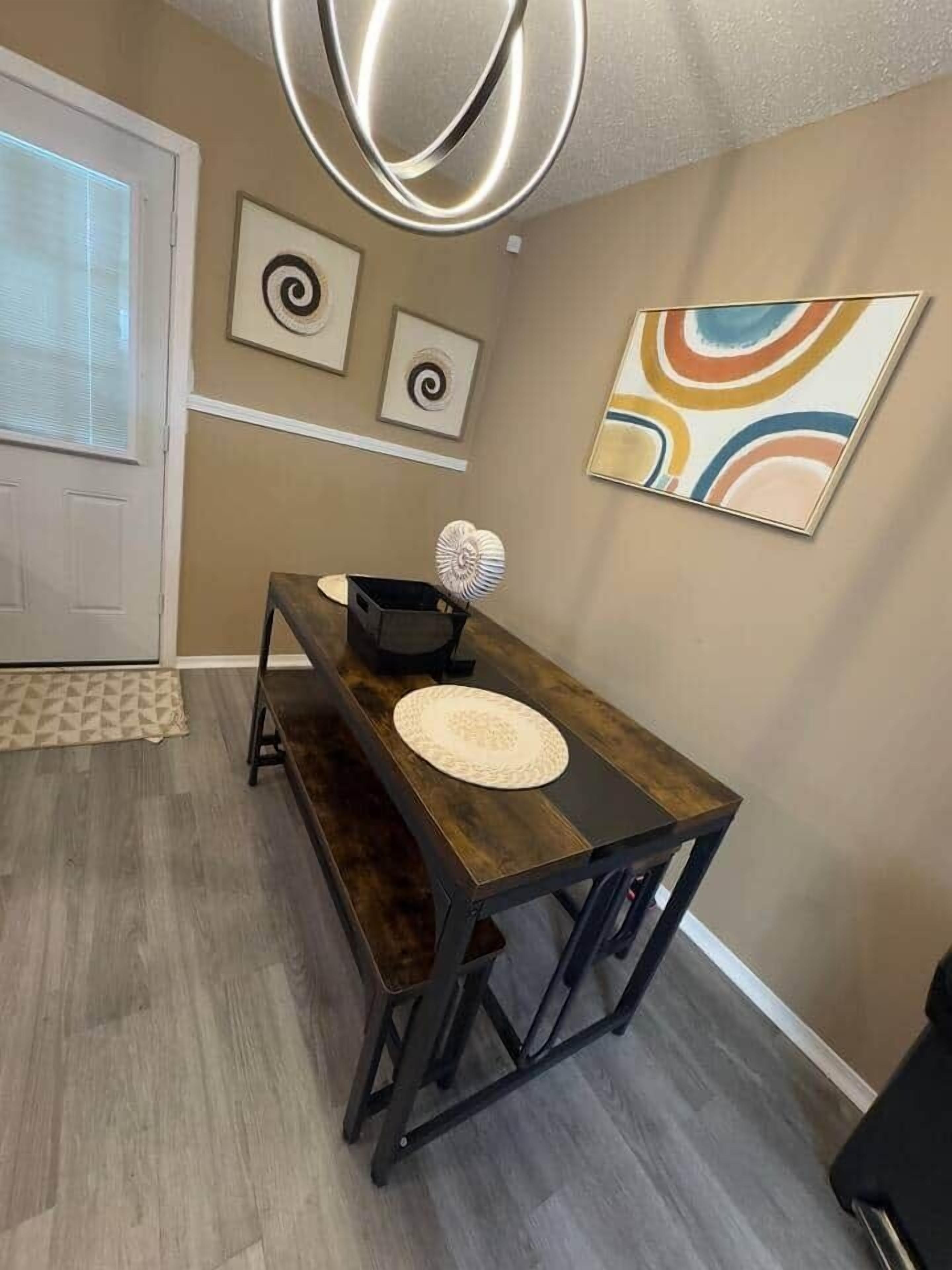 A dining area with a wooden table and benches, a decorative wall piece, and a patterned rug.