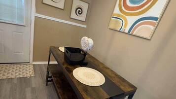 A dining area with a wooden table and benches, a decorative wall piece, and a patterned rug.