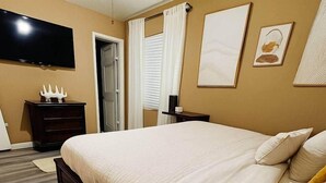 Une chambre d’hôtel dotée d’un grand lit, d’un téléviseur à écran plat fixé au mur, d’une table de chevet en bois et d’une porte donnant sur une autre pièce.