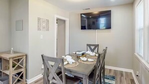 A dining area with a table set for four, a TV mounted on the wall, and a wooden sideboard.