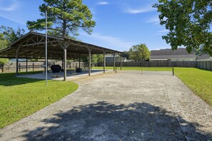 A covered outdoor area with a concrete path, a grill, and a picnic table.