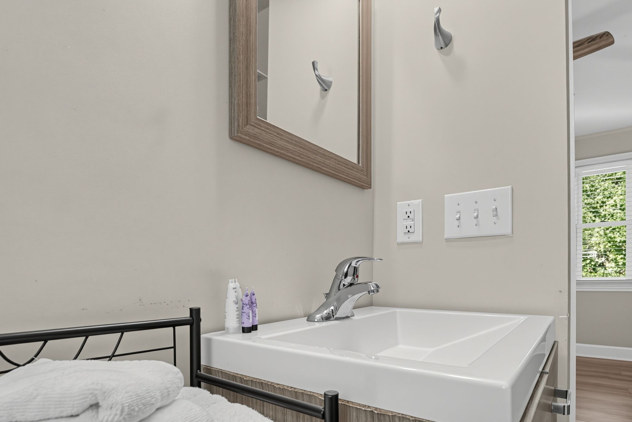 A modern bathroom with a large white bathtub, a mirror, a faucet, and a window with greenery outside.