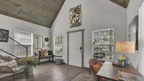 A spacious living room with a high ceiling, a staircase, and a large window with blinds. - Cactus Flower Lodge-20 min to Downtown-starlit Sky Views (Fredericksburg)