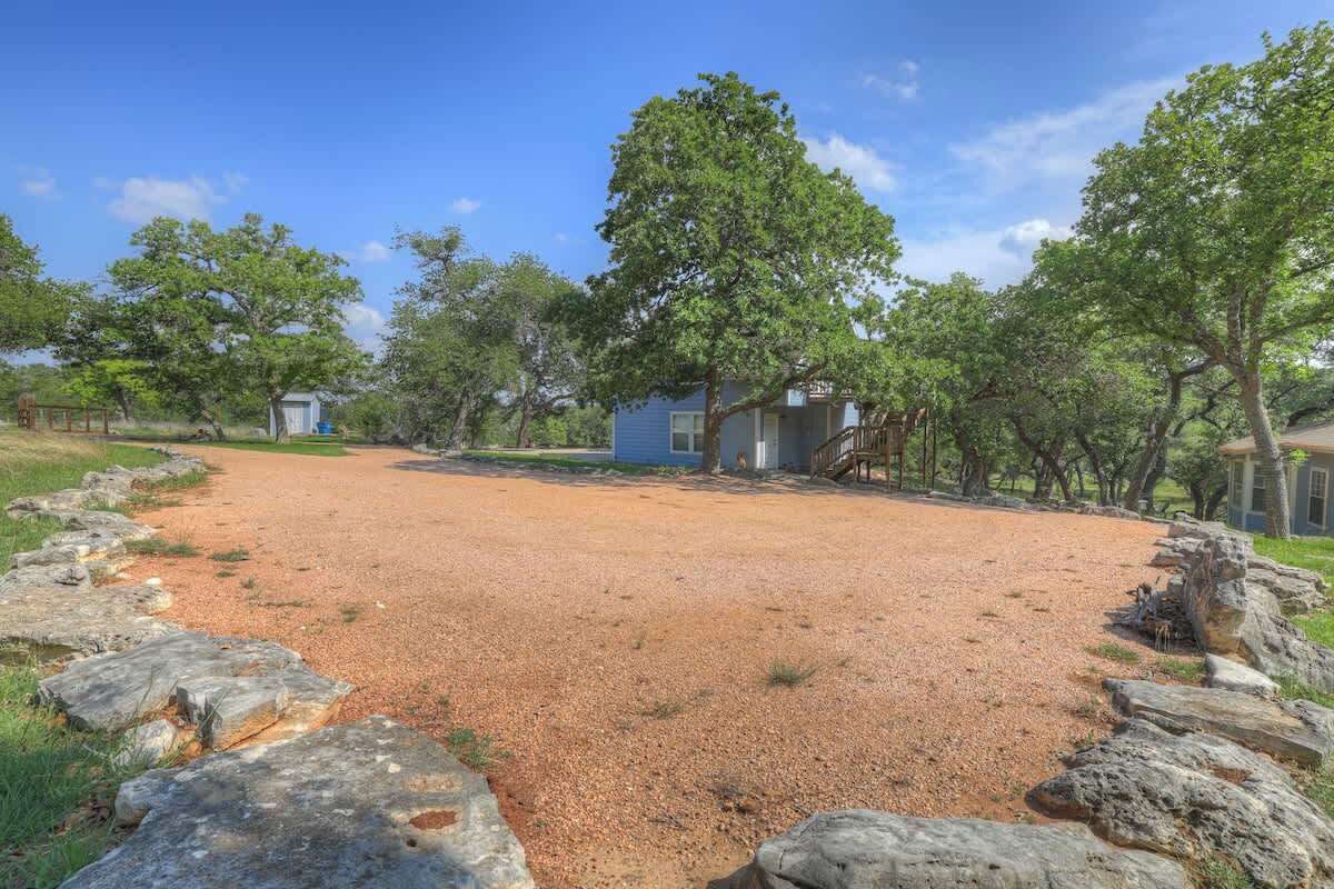 A gravel driveway leading to a blue house surrounded by trees.
