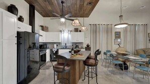 A modern kitchen with white cabinets, a black refrigerator, and a wooden island with bar stools. - Casa Blanca-swim Spa-steps to Main Street! (Fredericksburg)