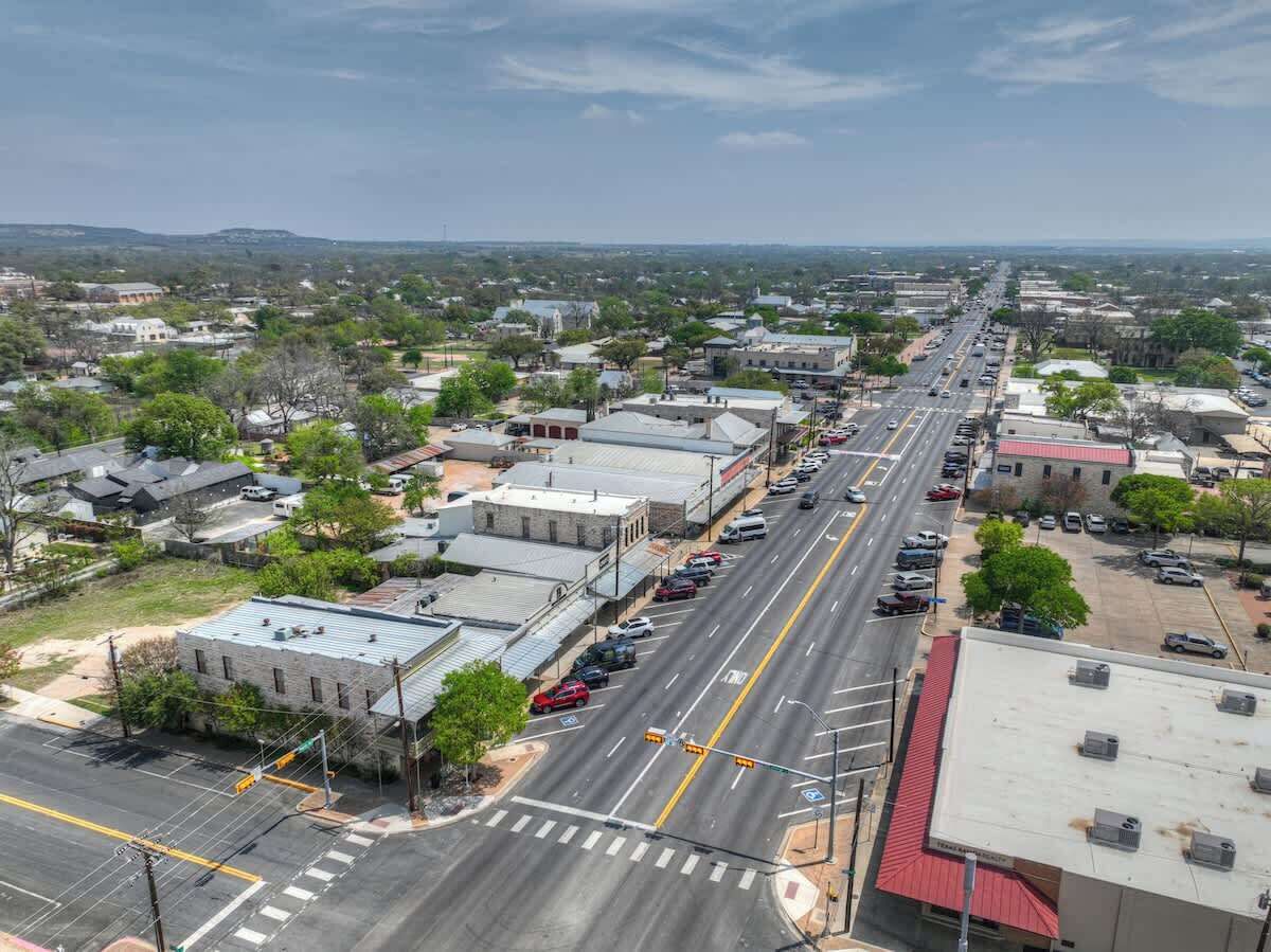 A wide street with buildings on both sides, a clear sky, and a distant view of hills.