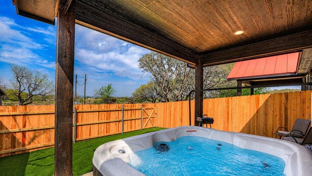 A hot tub with a wooden deck and a covered area, surrounded by a wooden fence and trees. - Cozy Casita With Hot Tub Six Minutes From Main Street (Fredericksburg)