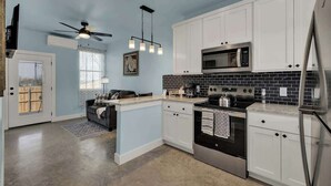 A modern kitchen with white cabinets, a black tiled backsplash, stainless steel appliances, and a ceiling fan. - Cozy Casita With Hot Tub Six Minutes From Main Street (Fredericksburg)