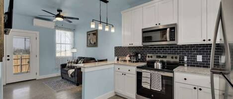 Una cocina moderna con armarios blancos, un revoque de azulejos negros, electrodomésticos de acero inoxidable y un ventilador de techo.