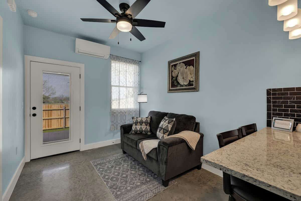 A room with a ceiling fan, a window with a view, a couch, a dining table, and a framed picture on the wall.