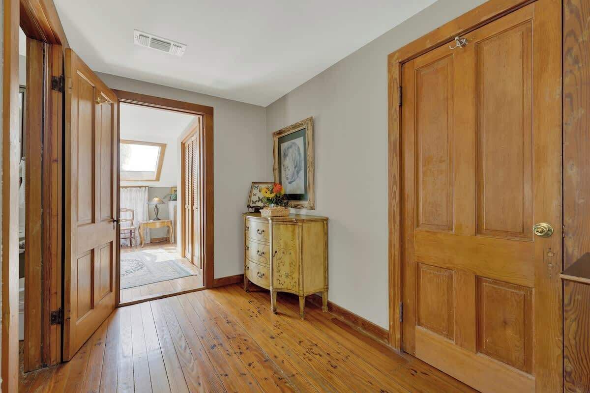 A hallway with wooden flooring, a wooden door, a vintage-style dresser, and a framed picture on the wall.