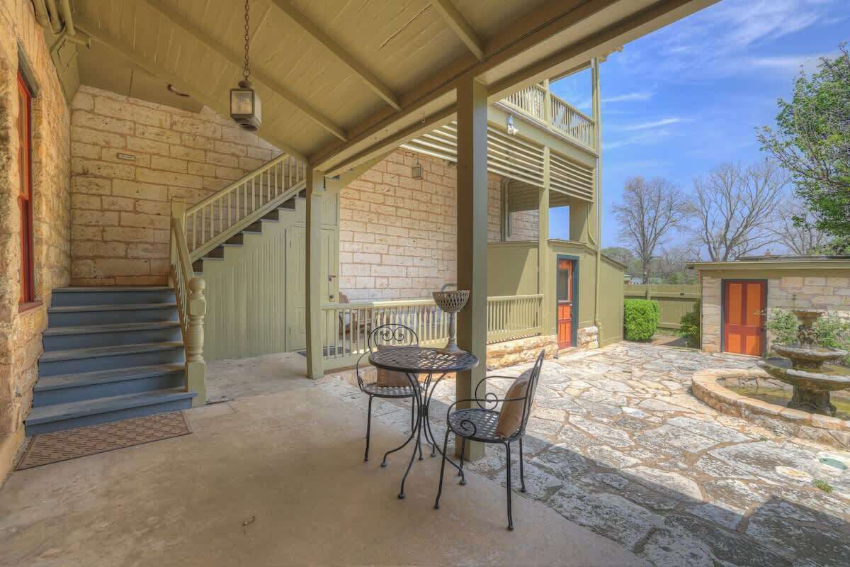 A covered patio with a stone floor, a table with chairs, and a staircase leading to a second level.