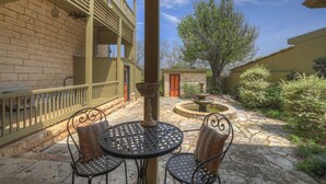 A courtyard with a stone floor, two metal tables with chairs, a small fountain, and a building with a balcony. - Fountain Suite-stay Right on Historic Main Street in the Heart of Fredericksburg (Fredericksburg)