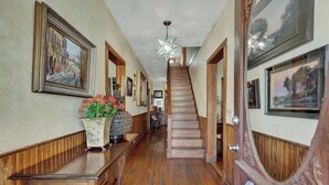A hallway with wooden floors, a staircase, and framed artwork on the walls.