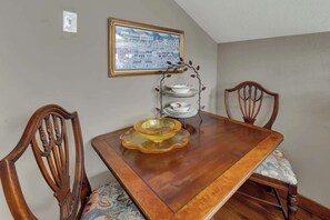 A dining table with a glass bowl centerpiece, wooden chairs, a wall-mounted shelf with dishes, and a framed picture. - Gillespie House-2 Suites-walk to Main St! (Fredericksburg)