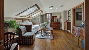 A loft-style room with a high ceiling, skylights, a bed, a sofa, a dining table, and a dresser.
