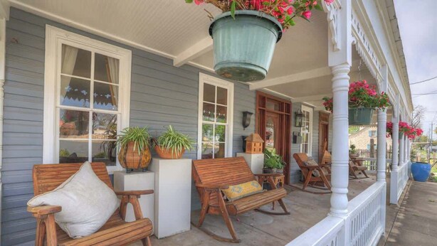 A porch with wooden rocking chairs, potted plants, and a hanging planter with flowers.