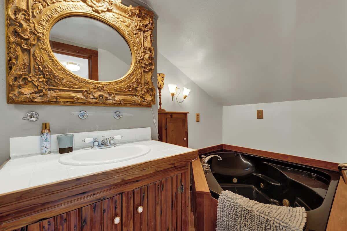 Un baño con tocador de madera, un espejo grande y decorativo, una bañera y un lavamanos blanco.